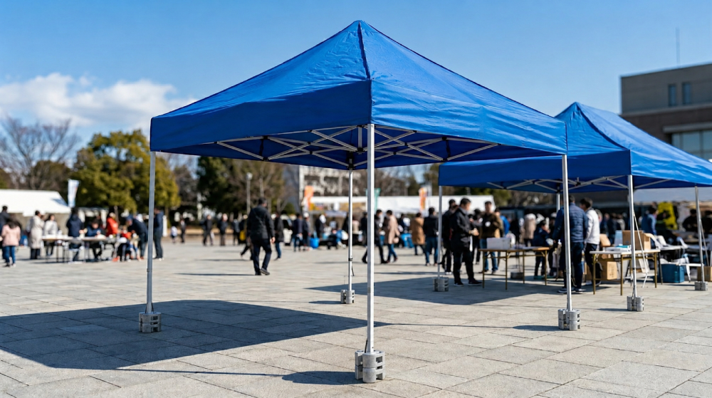 屋外イベント会場で、支柱足元に丸型の鋳物ウエイトを装着して風対策を行ったワンタッチテントの設置例